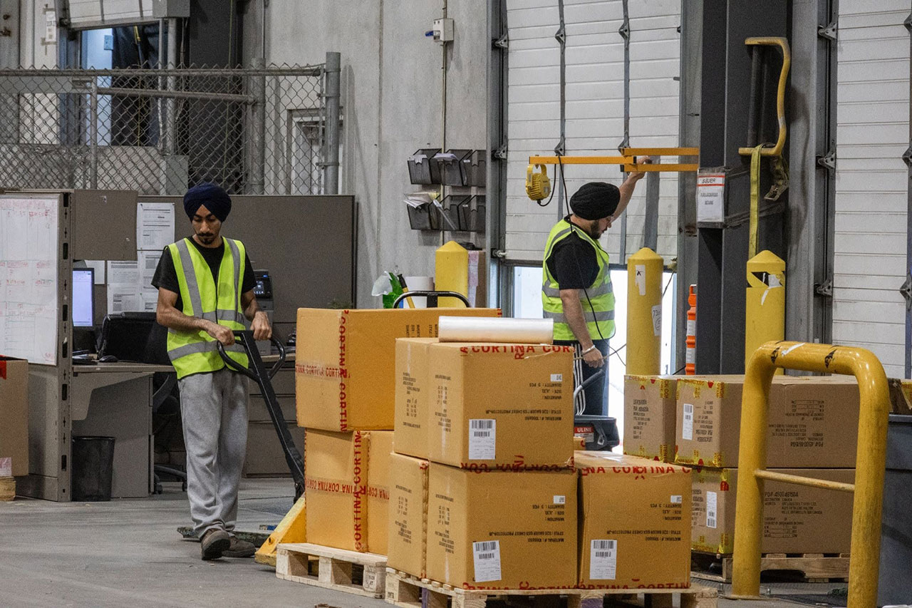 QRC warehouse staff moving a pallet of cartons with a pallet jack while a coworker works at a loading dock door QRC warehouse staff moving a pallet of cartons with a pallet jack while a coworker works at a loading dock door